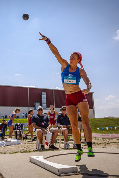 A woman throwing a shotput as other people watch from behind.