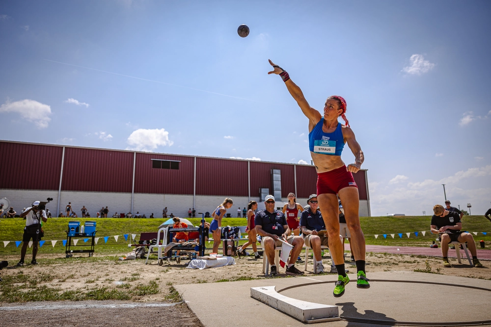 A woman throwing a shotput as other people watch from behind.